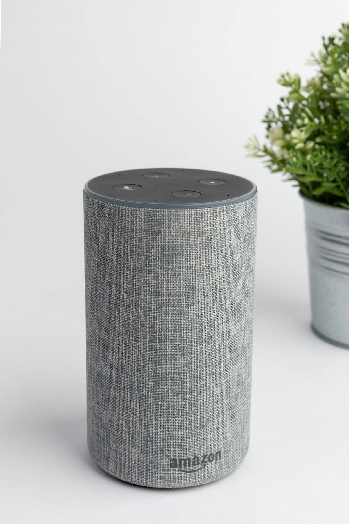 Fabric home speaker on a white shelf beside a plant